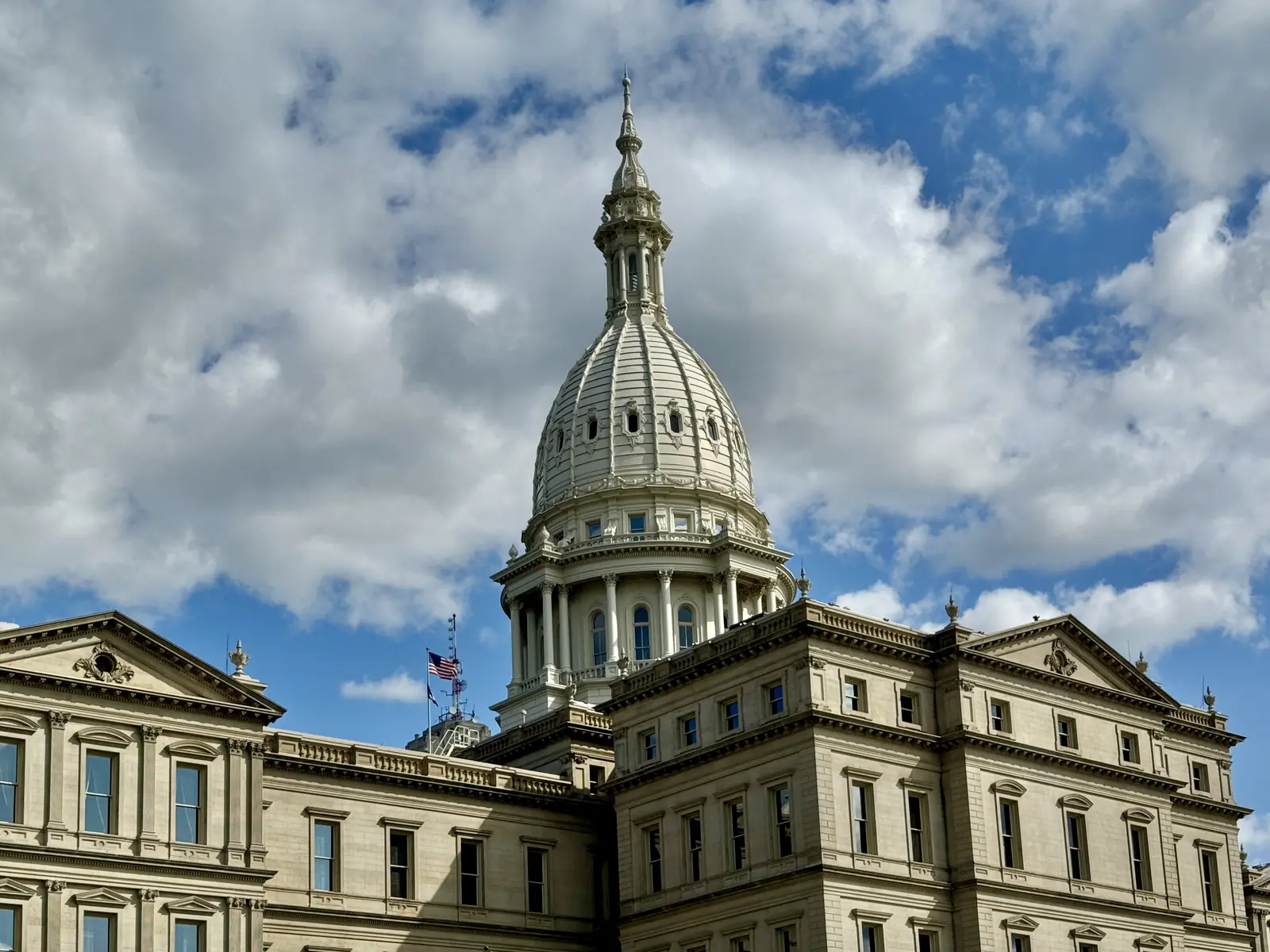 The dome and upper facade of the Michigan State Capitol building against a cloudy blue sky.