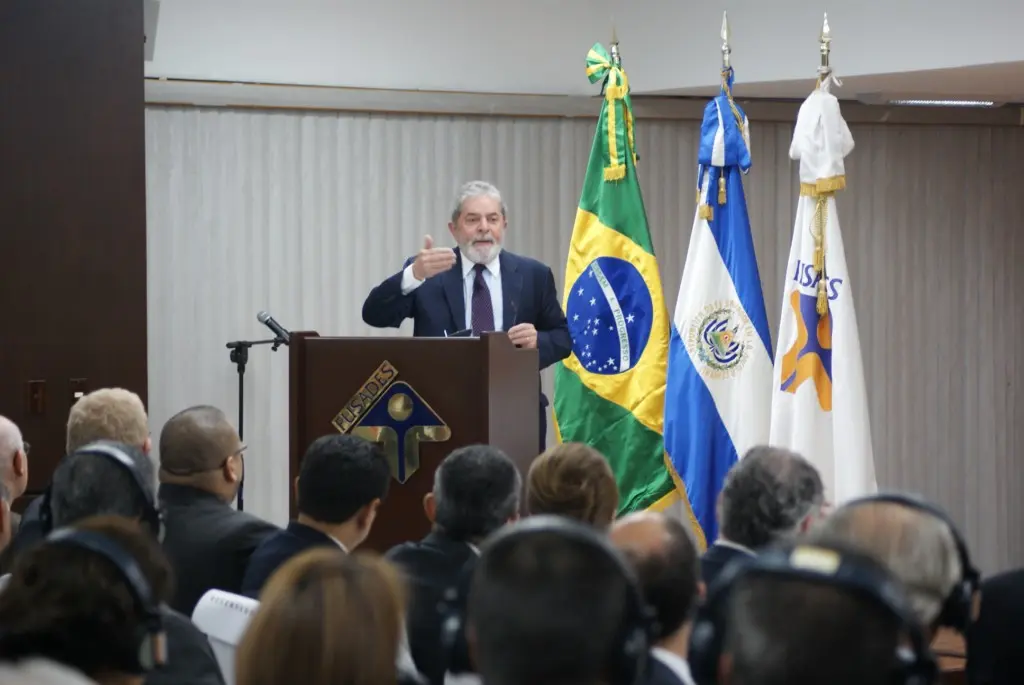 Luiz Inácio Lula da Silva speaking at a podium with the Brazilian flag and other banners behind him.
